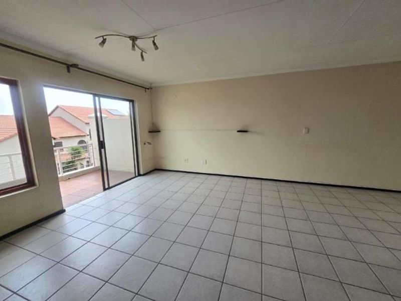 An empty, open-plan living area featuring neutral tiled flooring and a sliding glass door providing access to an outdoor balcony.