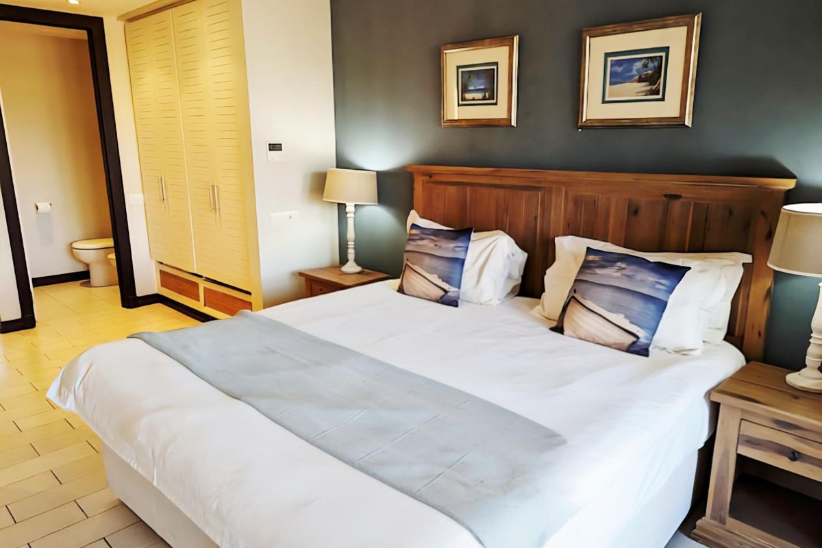 A well-maintained bedroom featuring built-in wooden cabinetry, tiled flooring, and an en-suite bathroom visible in the background.