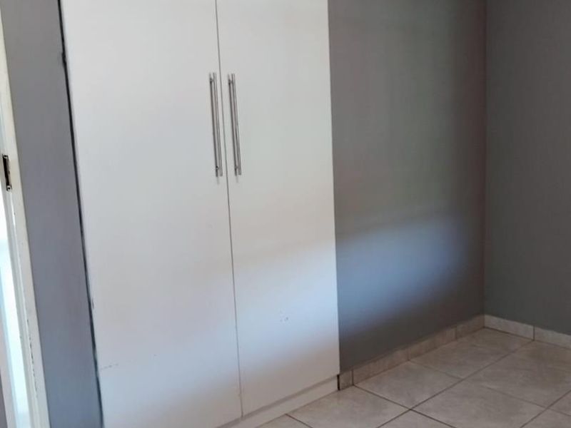 A simple bedroom featuring neutral grey walls, light ceramic floor tiles, and a white built-in wardrobe with modern handles.