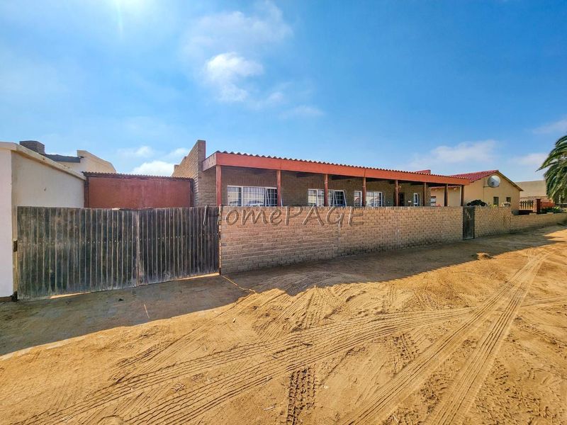 Front exterior view of a single-story house featuring a brick boundary wall, timber gate, and a covered patio area with a timber pergola.