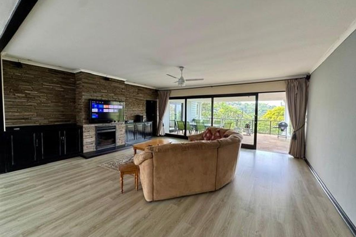 Spacious living room featuring a stone-clad fireplace wall, built-in cabinetry, and large sliding glass doors opening onto a covered patio with scenic views.
