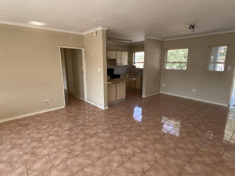 An open-plan living and kitchen area featuring tiled flooring, neutral walls, and functional kitchen cabinetry with a breakfast bar.