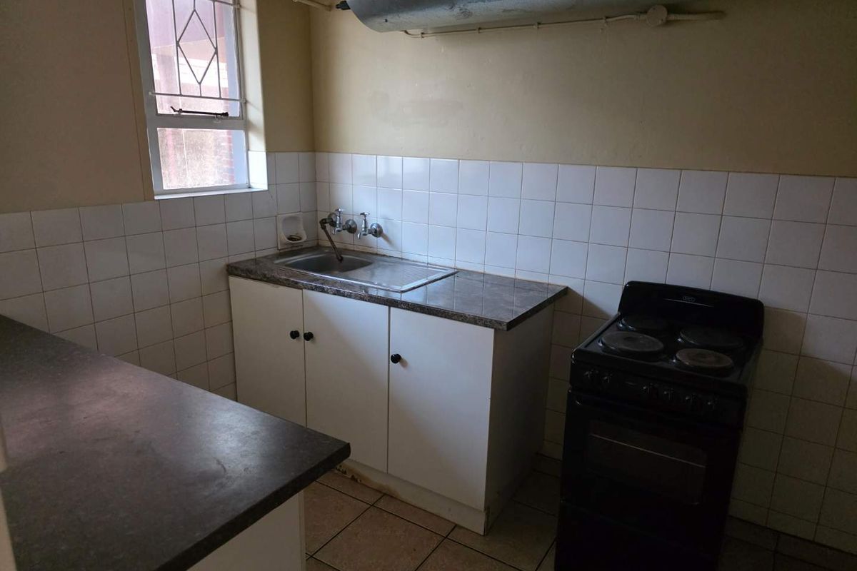 A compact kitchen featuring basic cabinetry, a stainless steel sink, tiled splashbacks, and a freestanding electric stove.