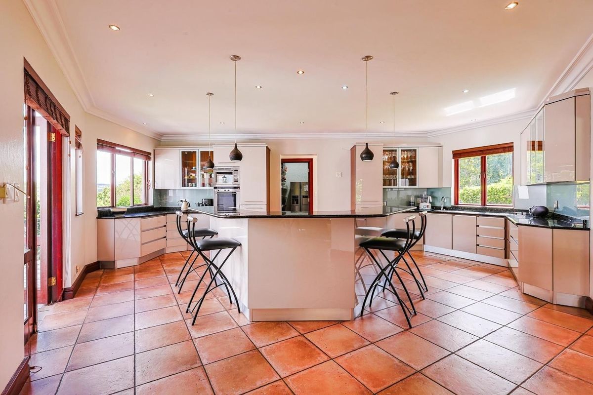 Spacious kitchen featuring a central island with breakfast bar, granite countertops, built-in oven, and ample cabinetry, finished with terracotta floor tiles.