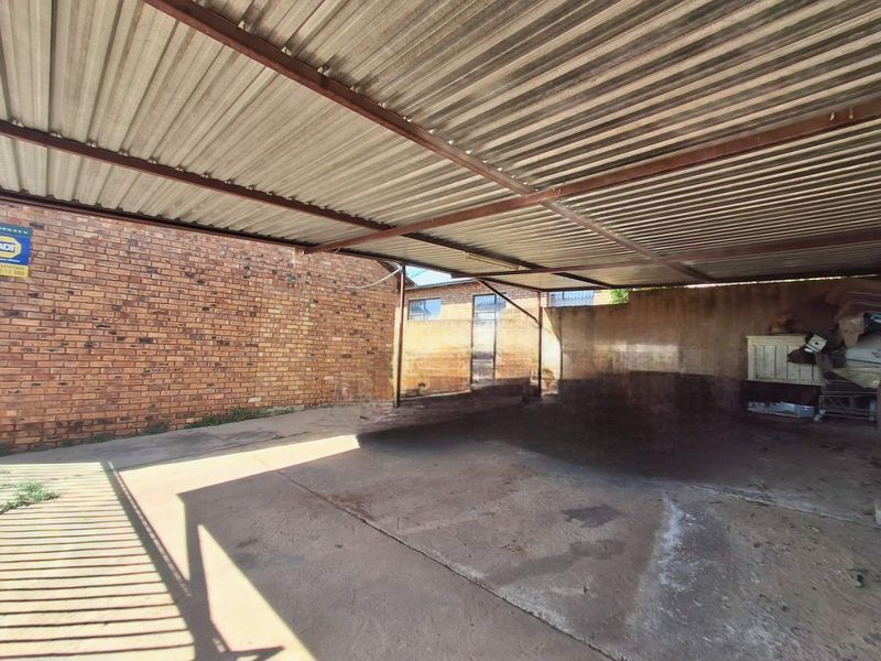 A covered outdoor parking area featuring a corrugated metal roof, steel support structure, and concrete flooring with exposed brick boundary walls.