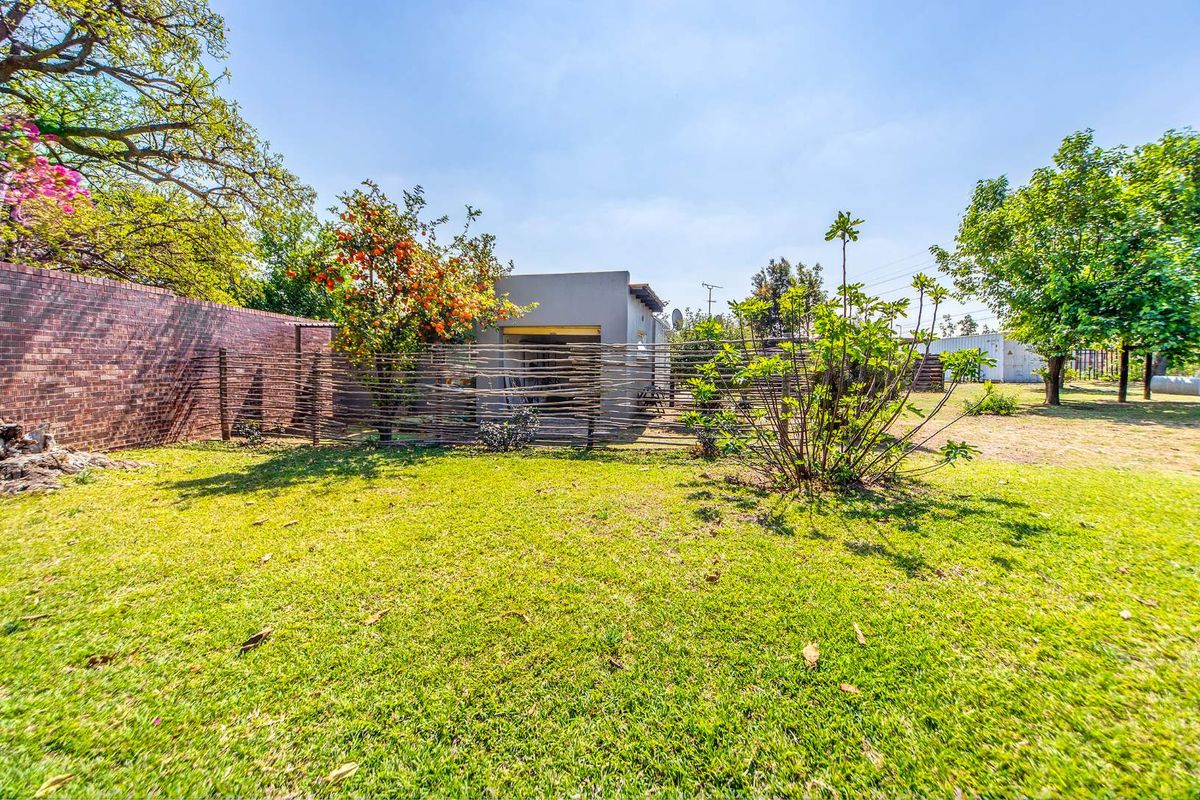 A spacious rear garden area featuring a well-maintained lawn, mature trees, and a brick boundary wall, leading to a detached outbuilding.