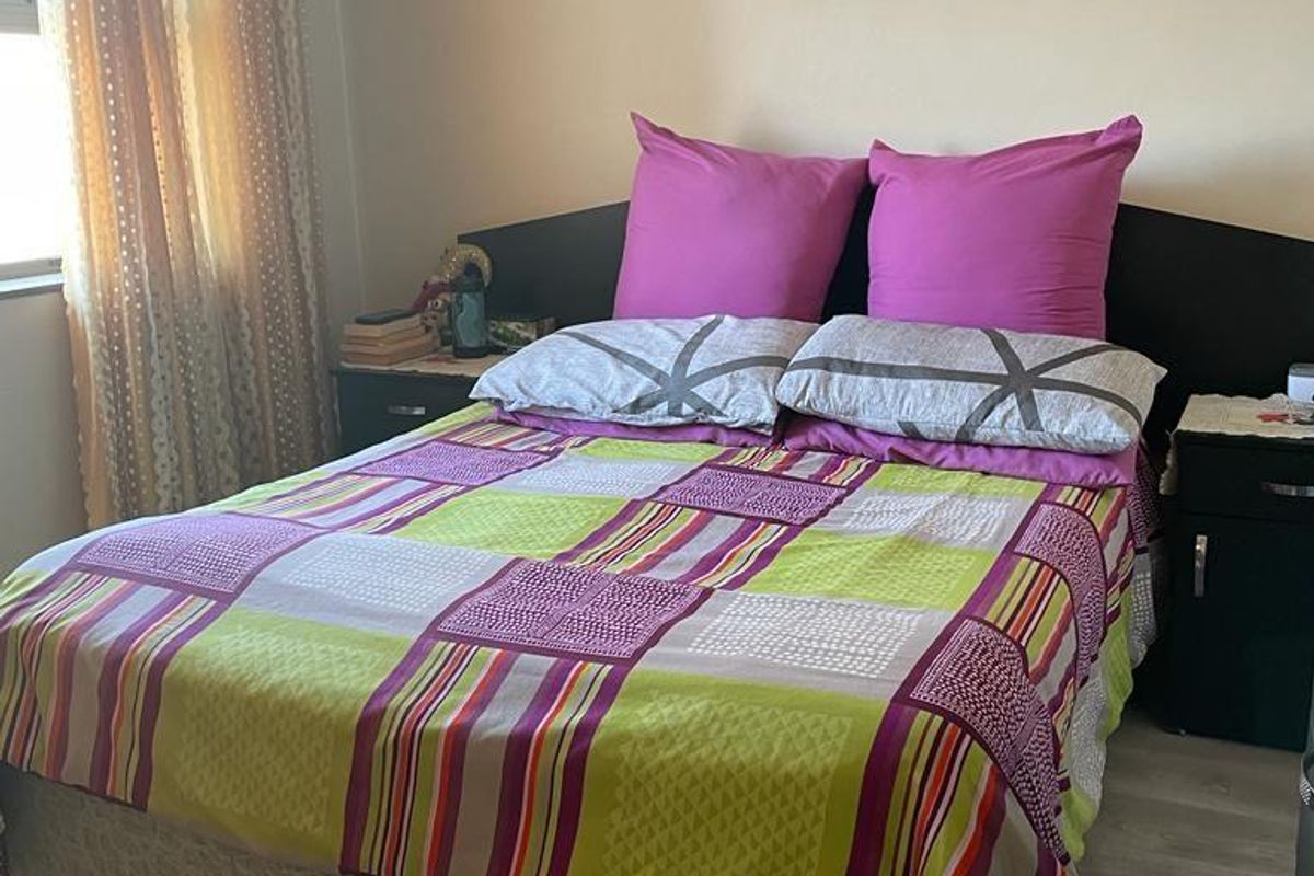A bedroom featuring light-toned laminate flooring and a window with curtain treatments.