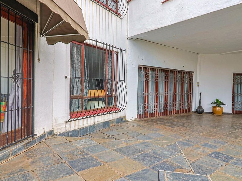 A covered patio area featuring slate tile flooring, security gates, and protective window bars, providing a functional outdoor space.