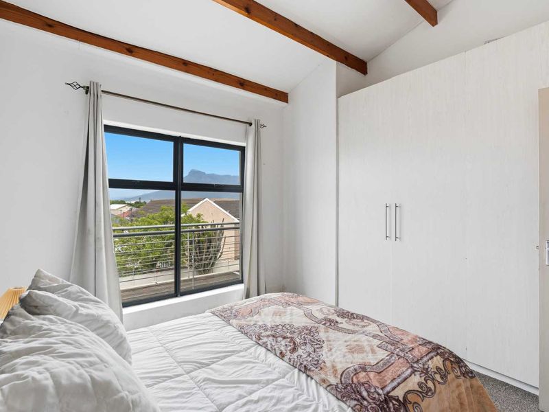 A bright bedroom featuring exposed timber ceiling beams, a large built-in wardrobe, and a window offering scenic mountain views.