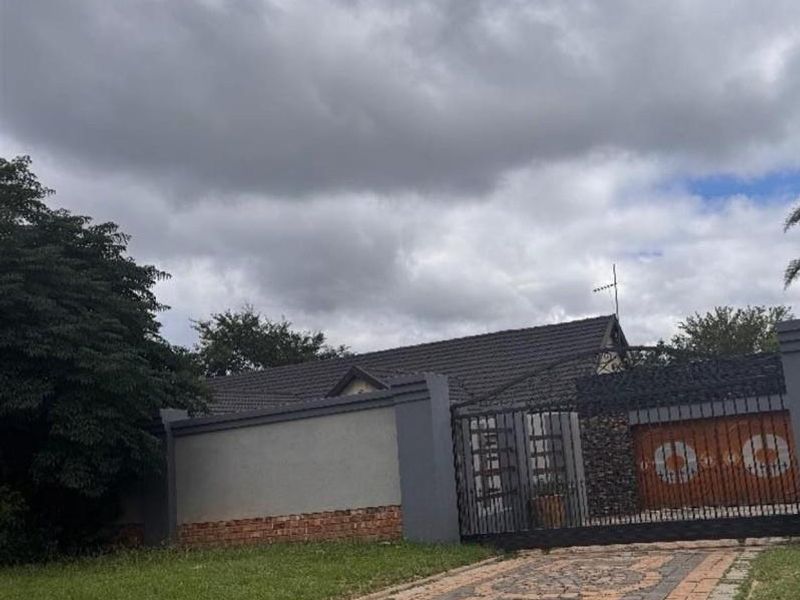Front exterior view of the property featuring a paved driveway, secure metal gate, and perimeter wall with a tiled roof structure.