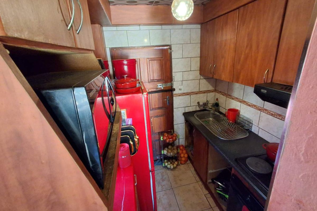 Compact kitchen featuring wooden cabinetry, tiled backsplash, and a functional sink area, offering potential for modernization and improved layout efficiency.