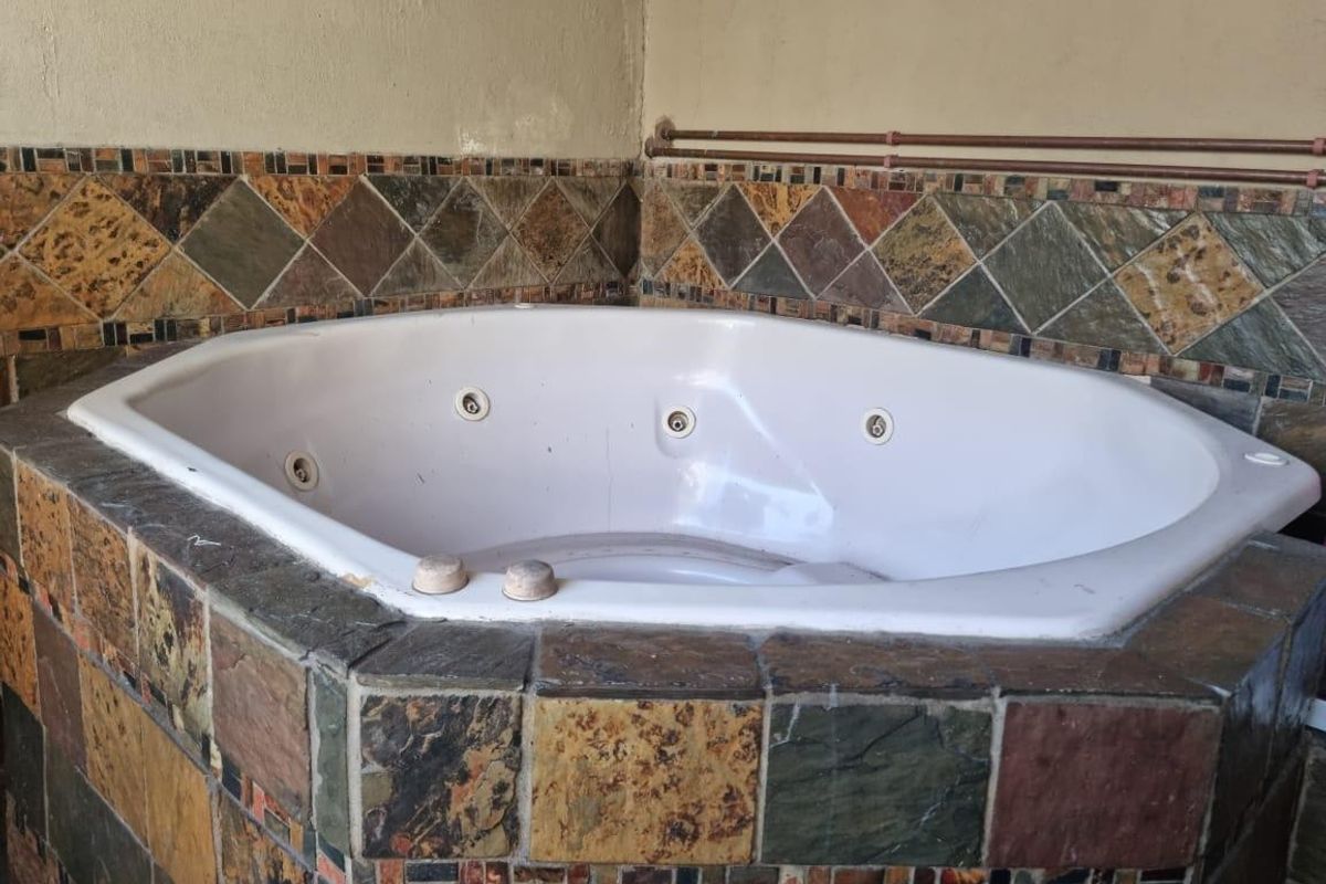 A corner spa bath featuring rustic slate tile cladding and exposed copper piping, requiring maintenance and cosmetic updates.