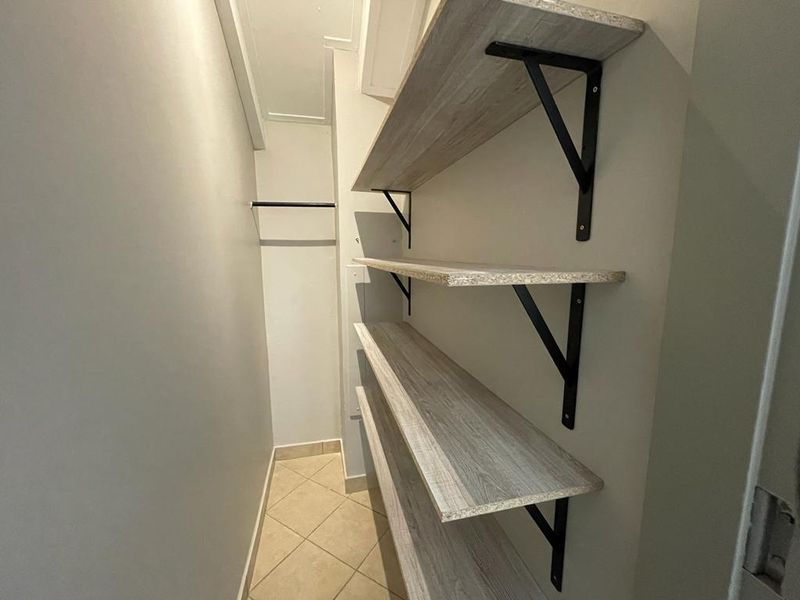A clean, functional utility or storage space featuring built-in wooden shelving with metal brackets and a hanging rail, finished with tiled flooring.