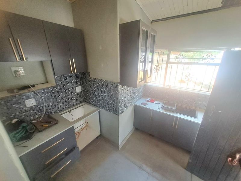 A compact kitchen featuring modern grey cabinetry, mosaic tile splashbacks, and a stainless steel sink, currently awaiting final appliance installation and finishing touches.