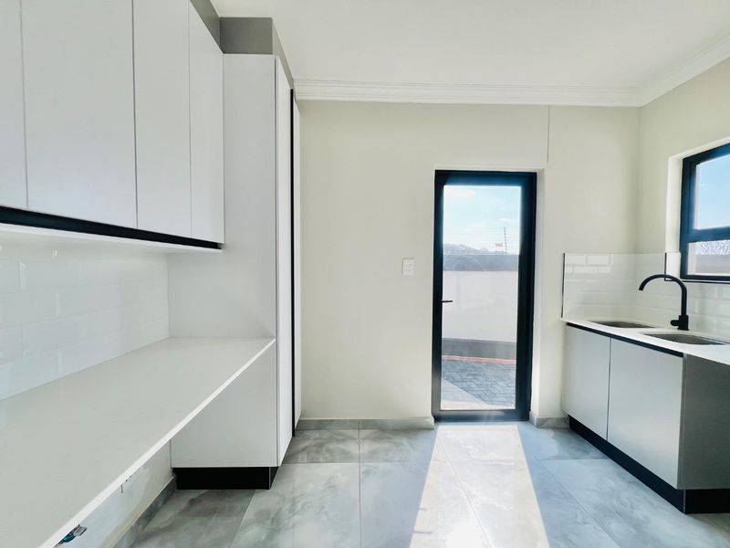 Modern scullery featuring sleek white cabinetry, stone countertops, subway tile backsplash, and a convenient glass door leading to the exterior.