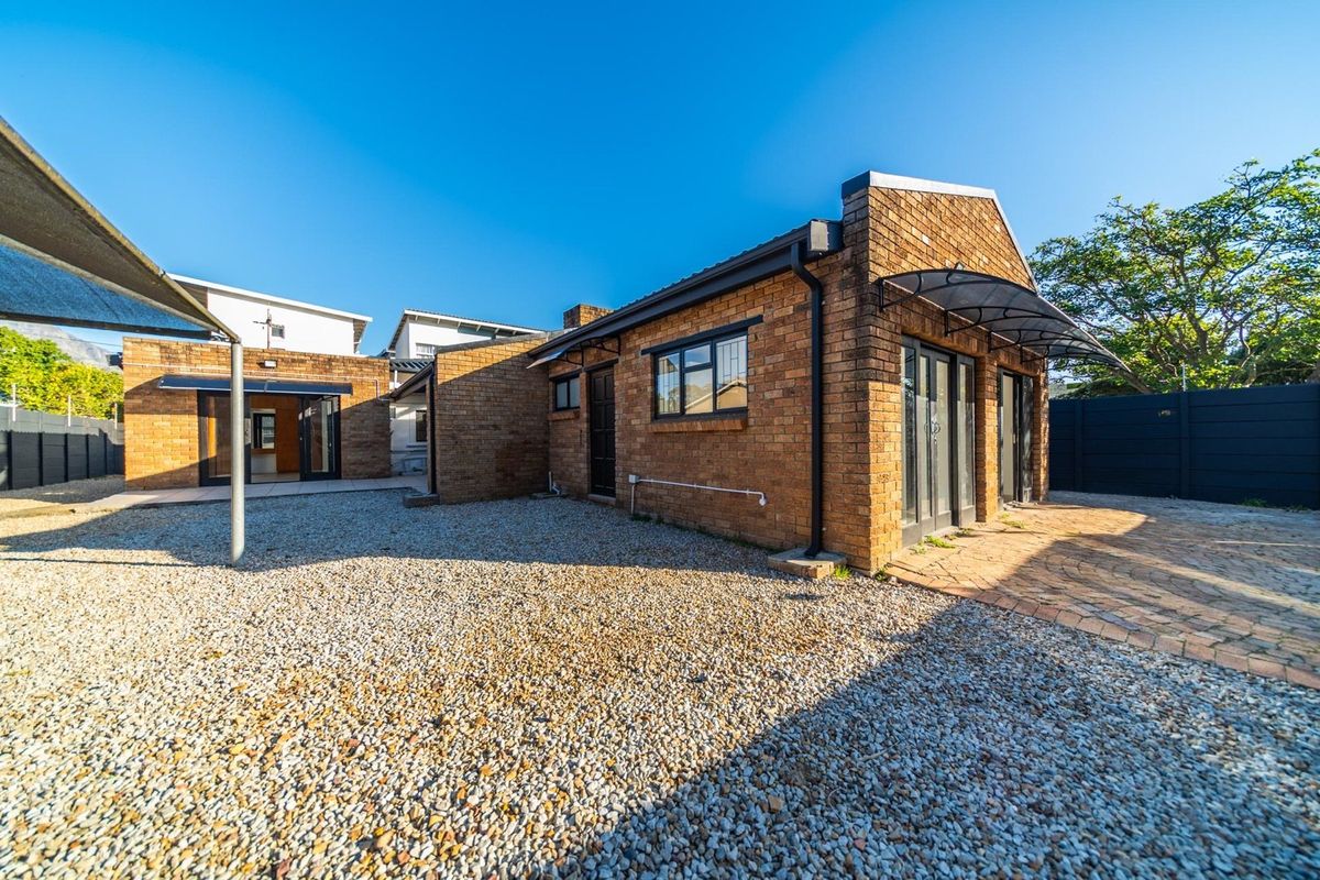 Rear exterior view of the apartment featuring a face brick facade, paved patio area, and a low-maintenance gravel courtyard with modern black aluminium fixtures.