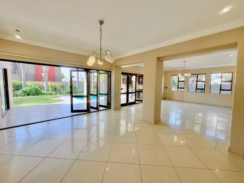 Spacious open-plan living area featuring polished tile flooring, crown molding, and large stacking glass doors providing seamless access to the outdoor pool area.