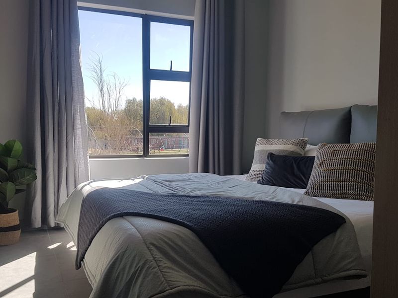 A well-lit bedroom featuring modern tiled flooring and a large window with views, providing a bright and comfortable living space.