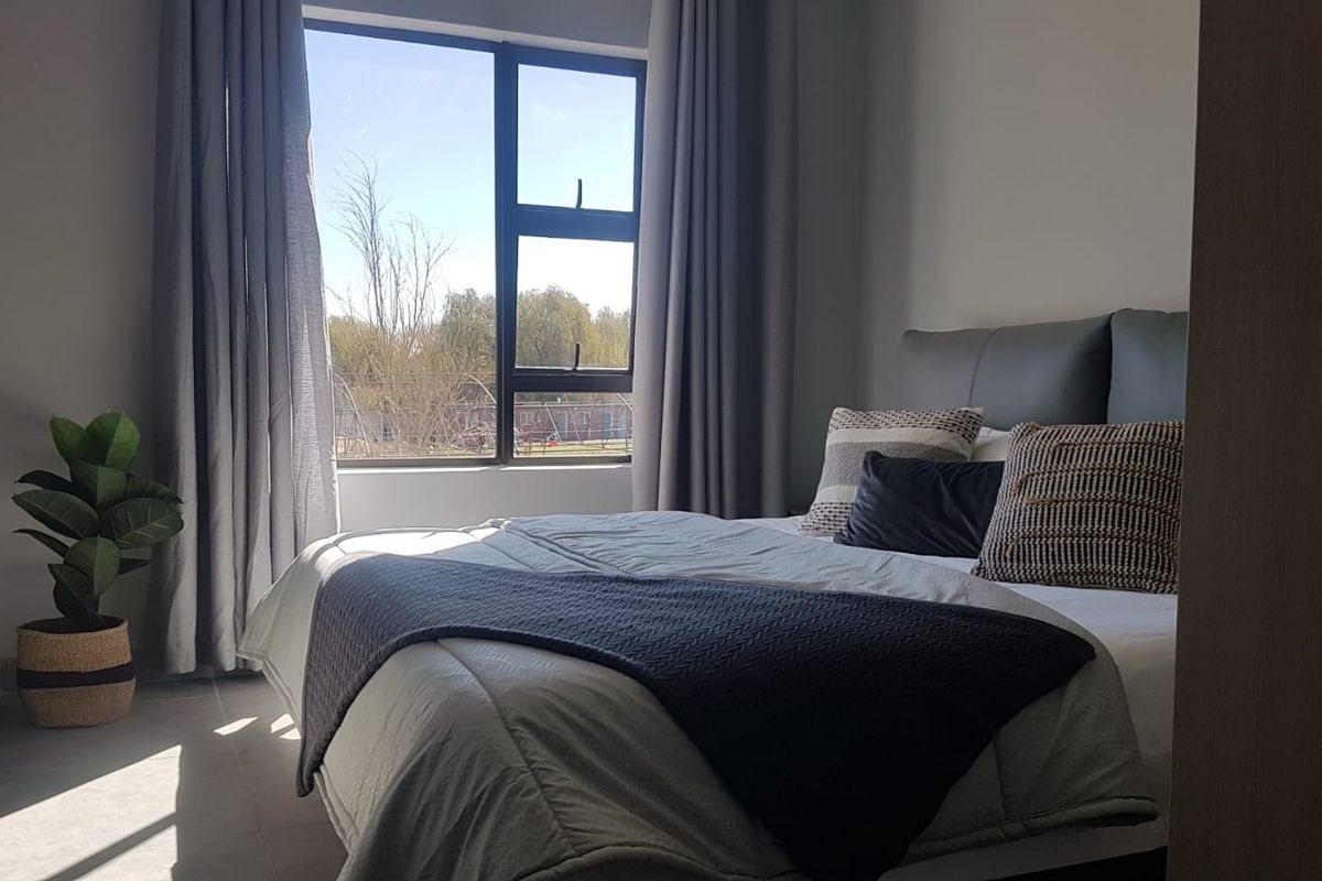 A well-lit bedroom featuring modern tiled flooring and a large window with views, providing a bright and comfortable living space.