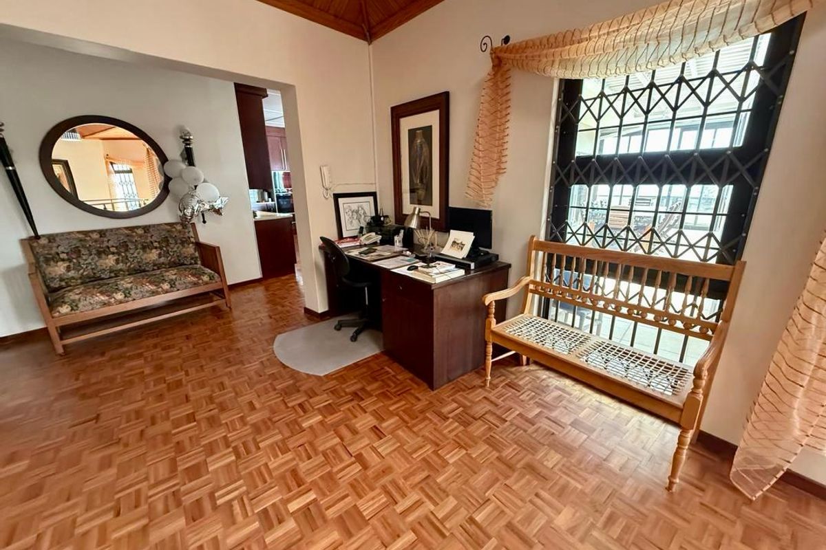 A multi-purpose living area featuring classic parquet flooring, a timber-paneled ceiling, and a security-gated window, with an adjacent view into the kitchen area.