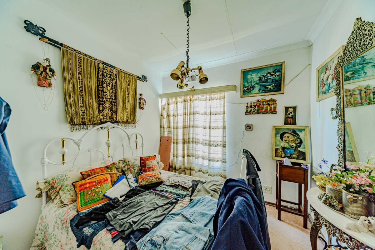 A bedroom featuring a central light fixture and window with curtain rail, showing signs of wear including visible wall cracks.