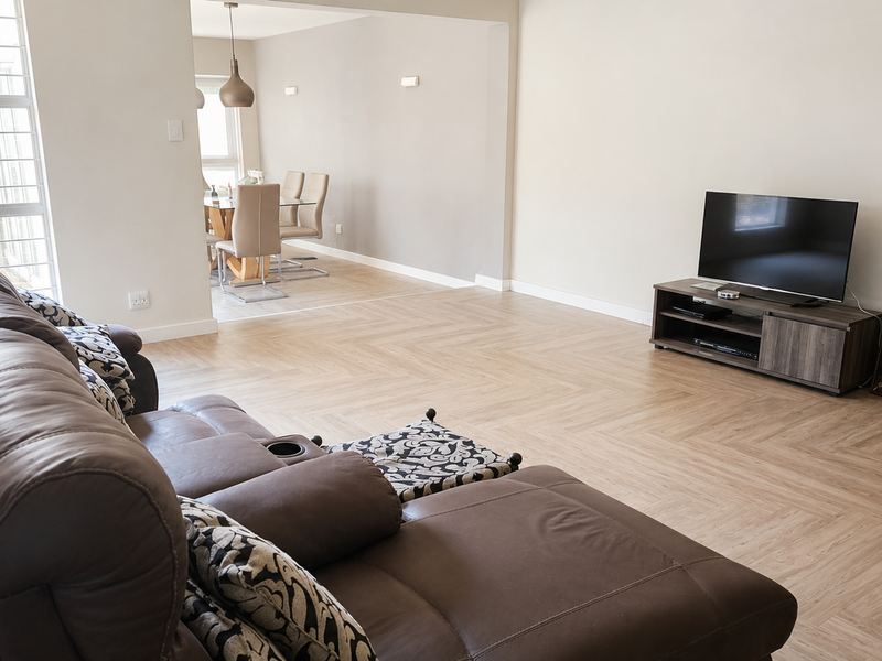 Spacious open-plan living and dining area featuring modern herringbone flooring, neutral walls, and abundant natural light through large aluminium-framed windows.