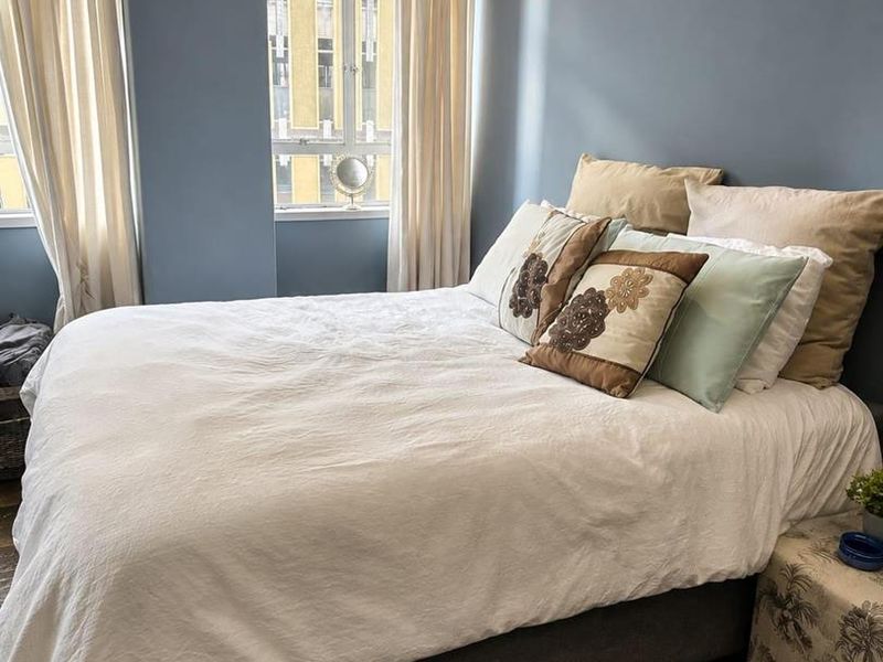 A well-lit bedroom featuring blue-toned walls, dark flooring, and a large window that allows for natural light.