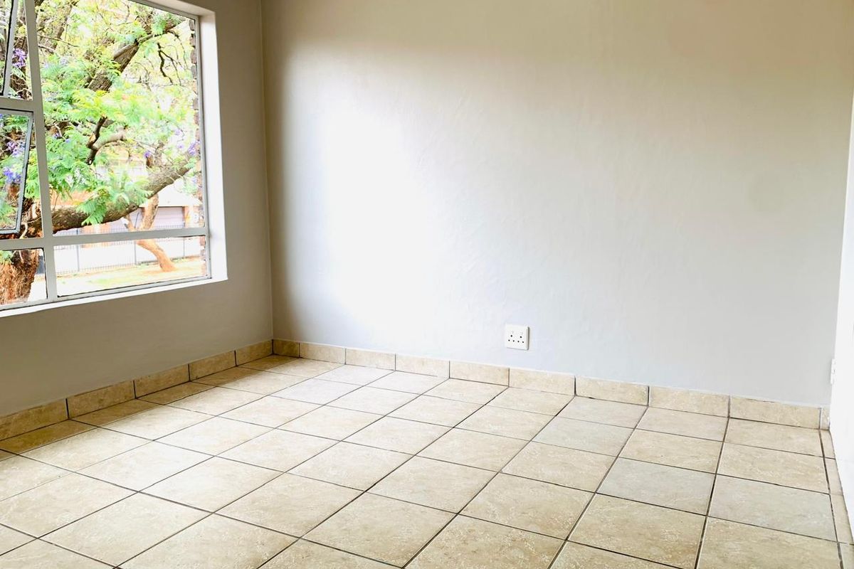 An empty bedroom featuring neutral tiled flooring, tiled skirting, and a large window providing natural light and a view of the outdoors.