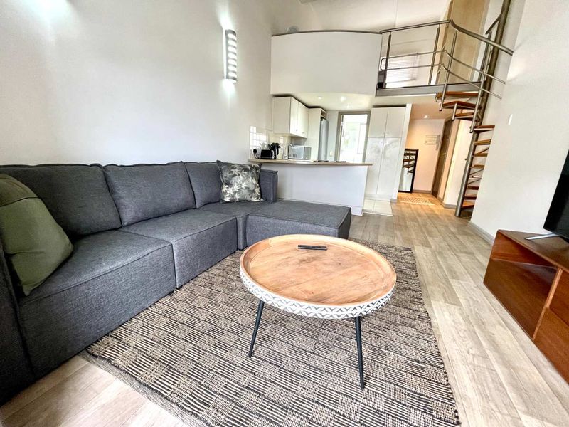 Open-plan living area featuring a spiral staircase leading to a mezzanine level, integrated kitchen cabinetry, and modern laminate flooring.