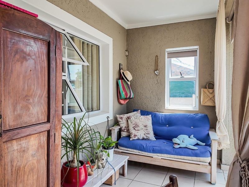 A covered patio area featuring tiled flooring, textured walls, and natural light through casement windows, suitable for a relaxed outdoor seating space.