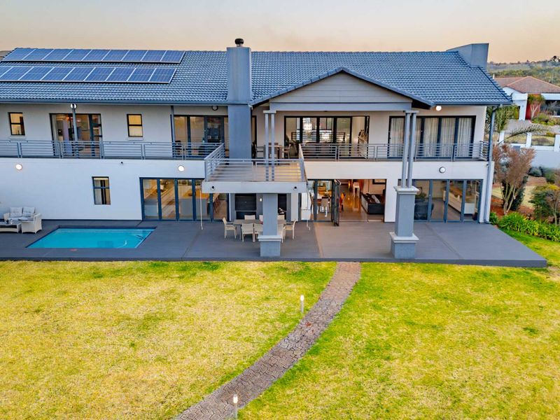 Aerial view of the rear elevation featuring a spacious patio, swimming pool, balcony, and solar panel installation on the tiled roof.