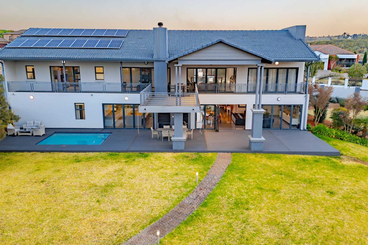 Aerial view of the rear elevation featuring a spacious patio, swimming pool, balcony, and solar panel installation on the tiled roof.
