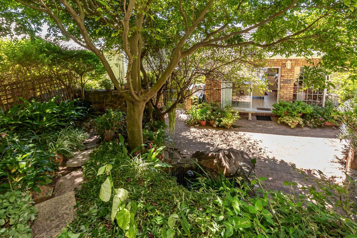 A private rear garden featuring a paved patio area, mature trees, and established landscaping, providing a tranquil outdoor space connected to the home.