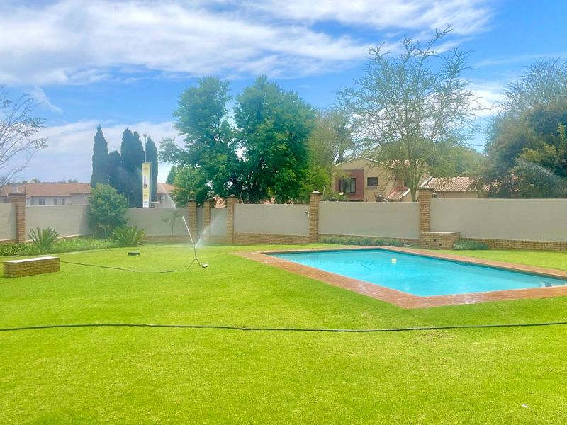 A spacious backyard featuring a well-maintained swimming pool, expansive lawn, and secure brick perimeter walling.
