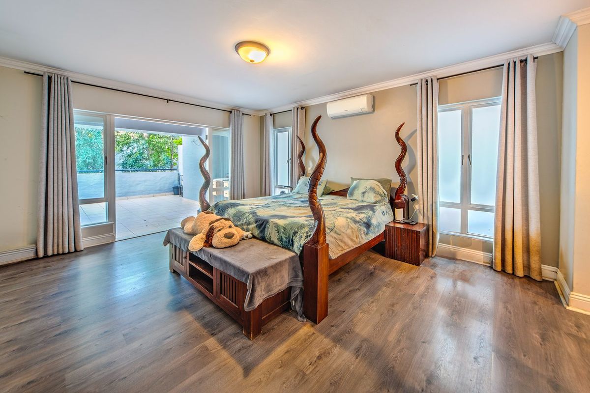 Spacious bedroom featuring laminate flooring, crown molding, a split-system air conditioner, and large sliding glass doors opening onto a private balcony.