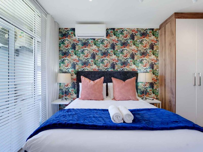 A well-maintained bedroom featuring a built-in wardrobe, split-system air conditioning, and stylish feature wallpaper, complemented by large windows with venetian blinds.