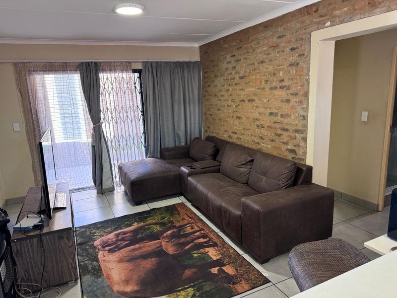 Living room featuring an exposed brick accent wall, tiled flooring, and a sliding glass door providing access to the exterior.
