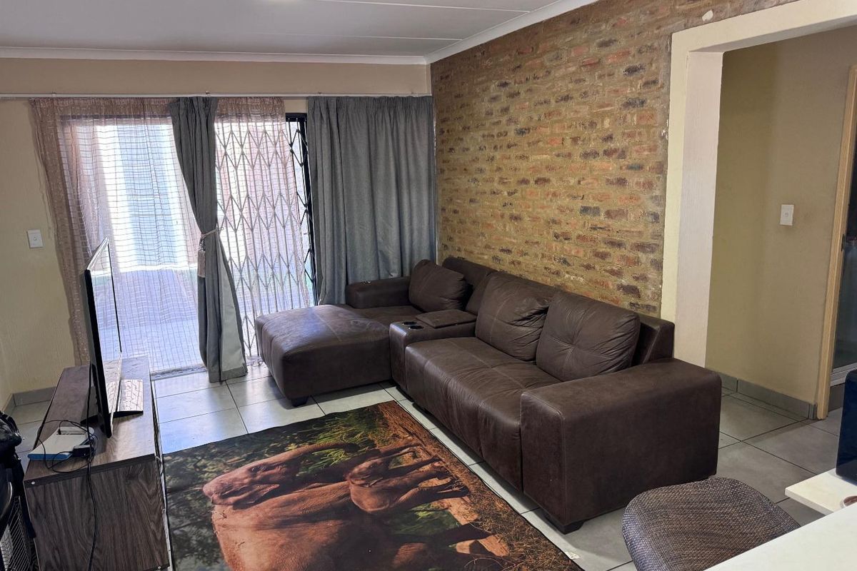 Living room featuring an exposed brick accent wall, tiled flooring, and a sliding glass door providing access to the exterior.