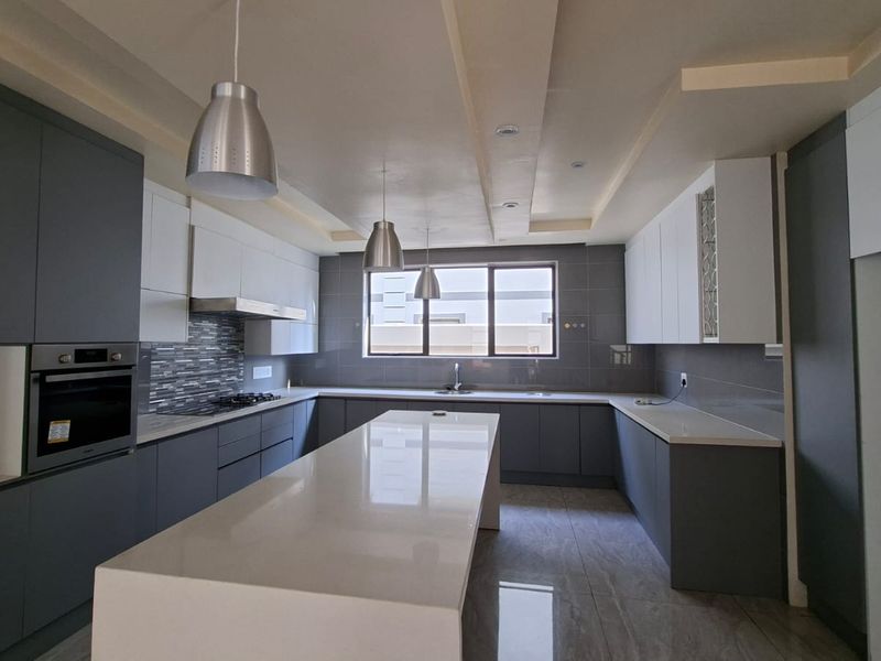 Modern, spacious kitchen featuring sleek grey and white cabinetry, a large central island with stone countertops, and high-quality built-in appliances.
