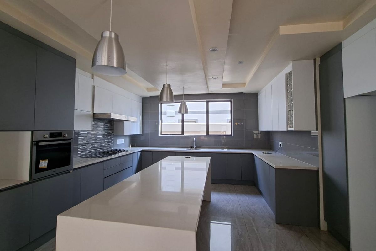 Modern, spacious kitchen featuring sleek grey and white cabinetry, a large central island with stone countertops, and high-quality built-in appliances.