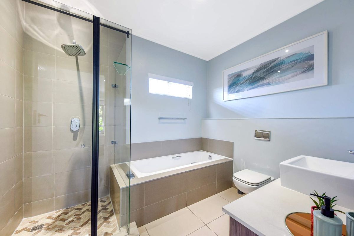 Modern bathroom featuring a walk-in shower with glass screen, built-in bathtub, wall-mounted toilet, and a sleek vanity basin with contemporary tiling.