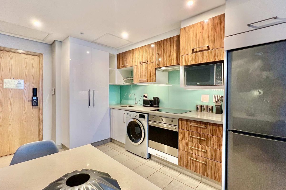 Modern kitchen featuring wood-grain cabinetry, integrated appliances including a washing machine and oven, and a sleek glass splashback.