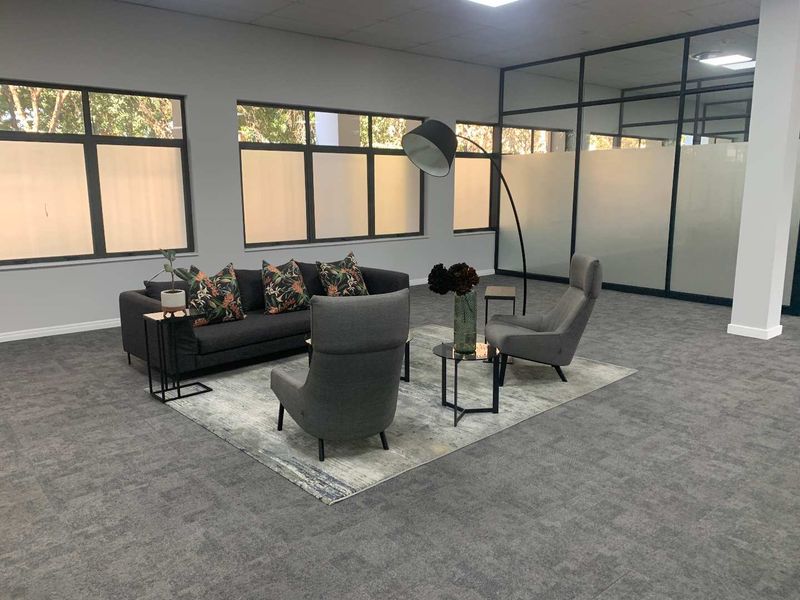 Modern office space featuring carpet tiles, recessed lighting, large aluminium windows, and a contemporary glass partition wall for a professional work environment.