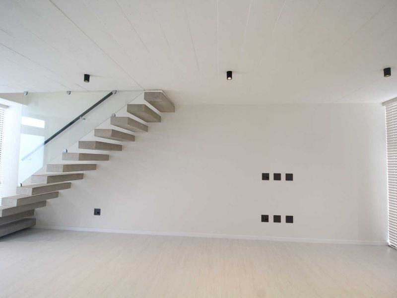 Modern open-plan living area featuring a striking floating concrete staircase with glass balustrade, recessed lighting, and clean minimalist finishes.