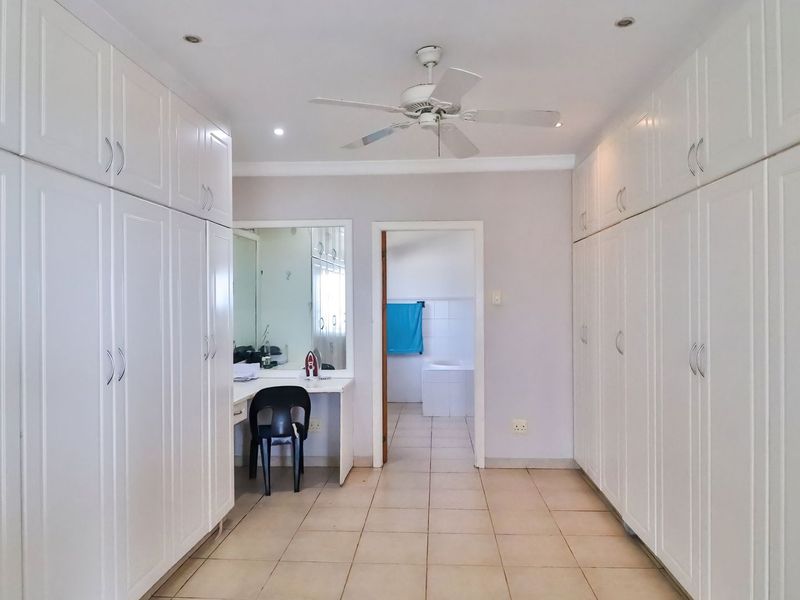 Spacious dressing area featuring extensive built-in cabinetry, a vanity station, and direct access to an en-suite bathroom.
