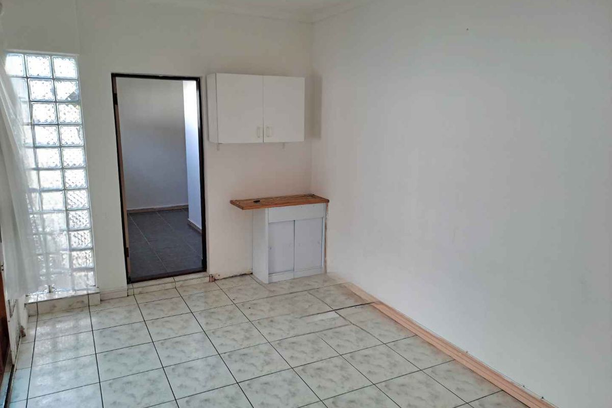 A small, empty utility or kitchen area featuring tiled flooring, a glass block window, and basic built-in cabinetry.