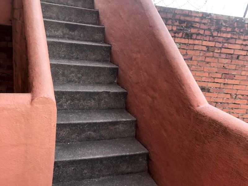 Exterior concrete staircase leading to an upper level, featuring a brick boundary wall with security razor wire.