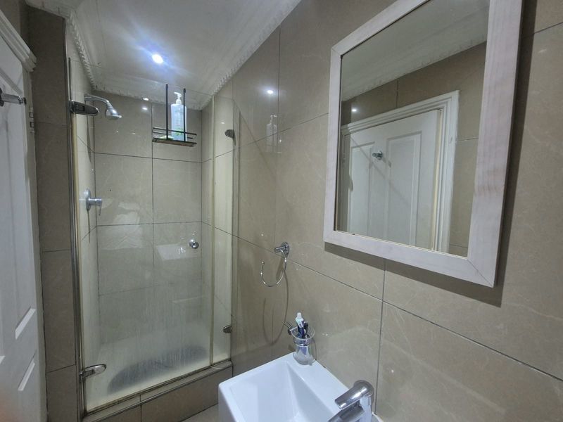 A compact bathroom featuring a glass-enclosed shower, wall-mounted basin with chrome fixtures, and neutral wall tiling.