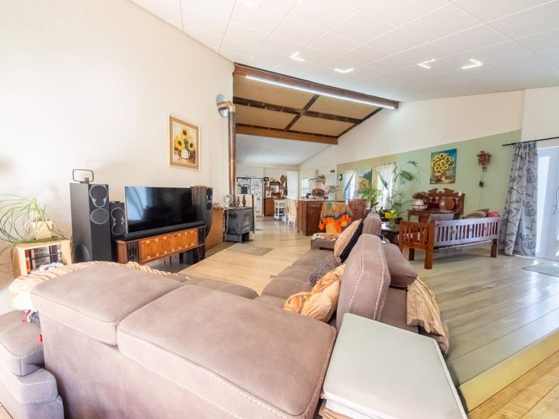 Spacious open-plan living area featuring a wood-burning stove, exposed timber ceiling beams, and a mix of tiled and laminate flooring with direct outdoor access.