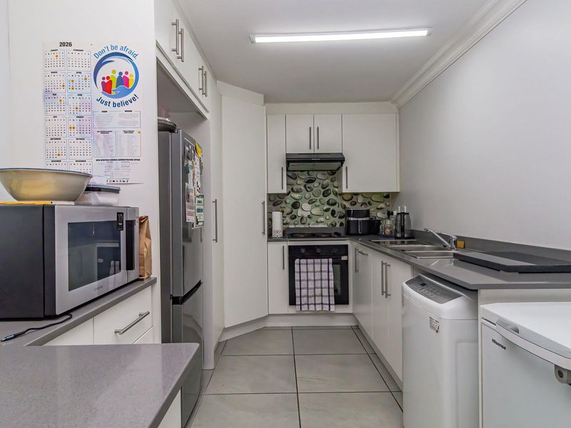 A functional kitchen featuring white cabinetry, stone-look splashback, integrated oven with extractor fan, and durable tiled flooring.